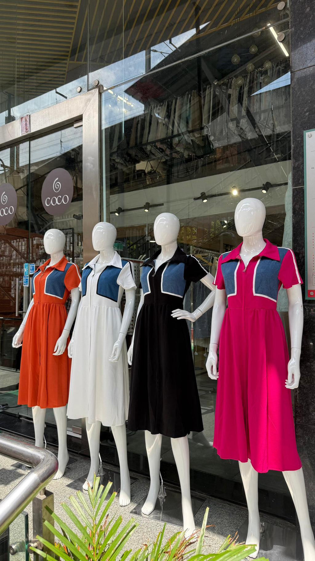 Mannequins wearing colorful dresses in front of a store window.